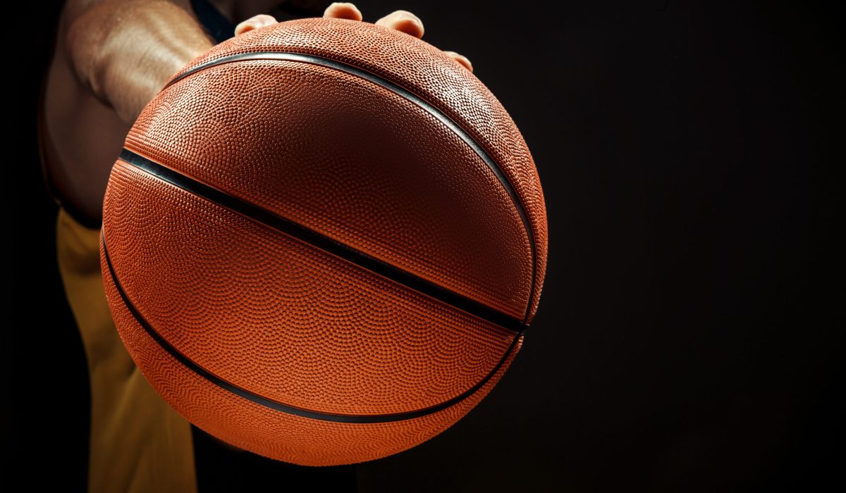 The silhouette view of a basketball player holding basket ball on black background. The hands and ball close up